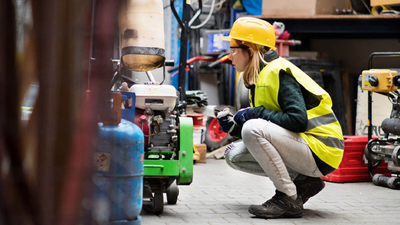A personal crouching to inspect a piece of equipment in a workshop