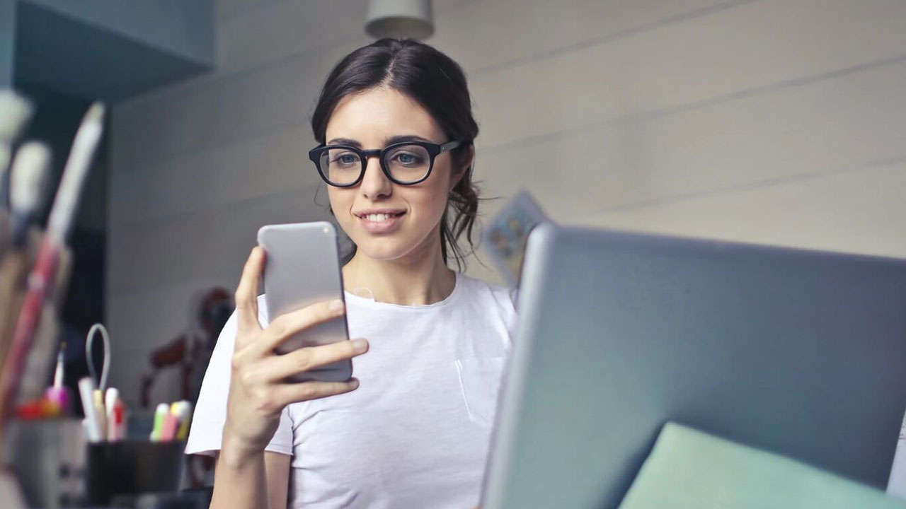 A person looking at their phone while working on a laptop